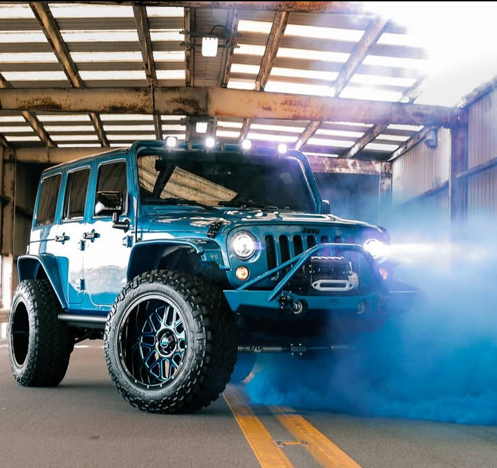 Teal lifted Jeep with illuminated headlights in the Ultimate Rides shop